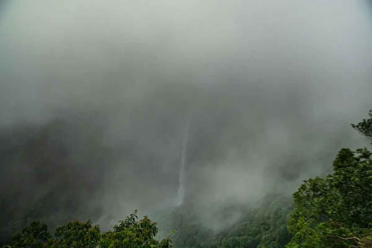 A waterfall half hidden in thick monsoon cloud over the green hills around Cherrapunji