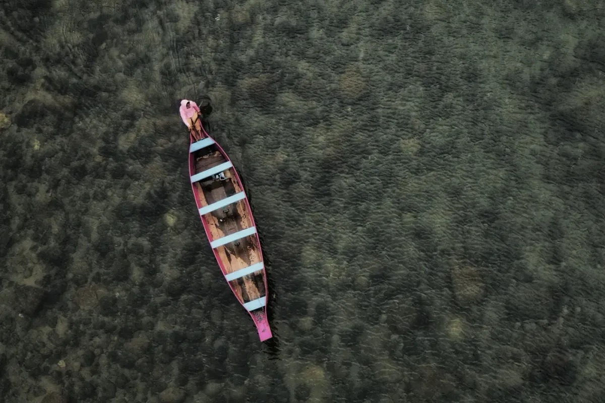 A wooden boat on the Umngot river at Dawki appearing to float above the visible pebbled riverbed