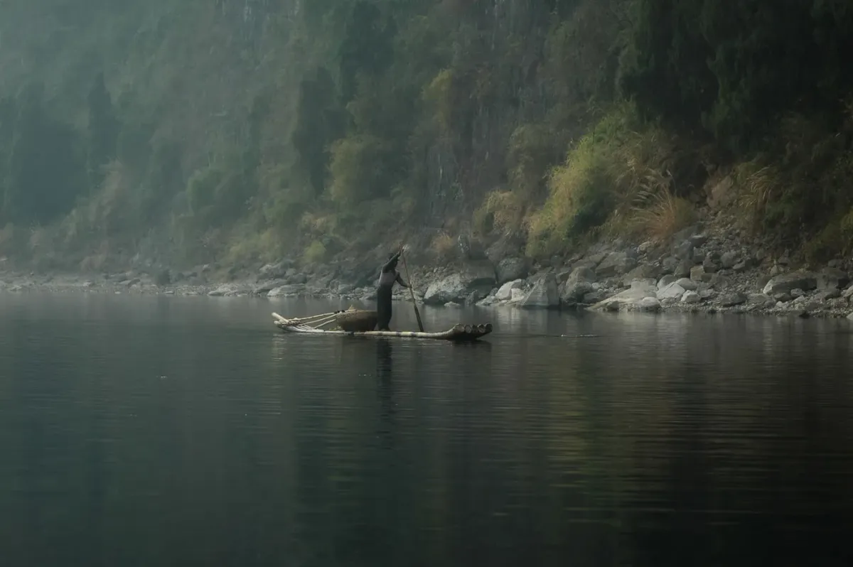 A lone boatman poling a bamboo raft through morning mist on the Umngot river at Shnongpdeng