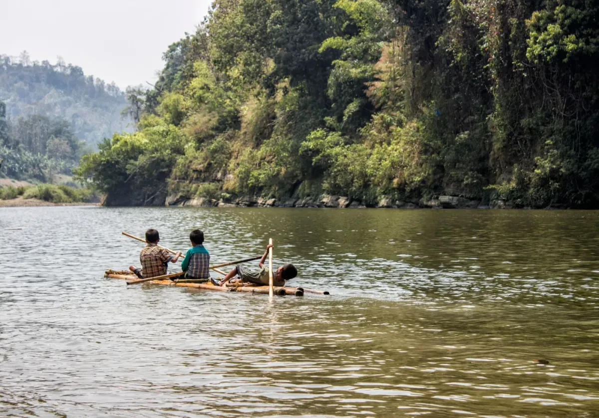 Three young people paddling a bamboo raft on the Umngot river at Shnongpdeng